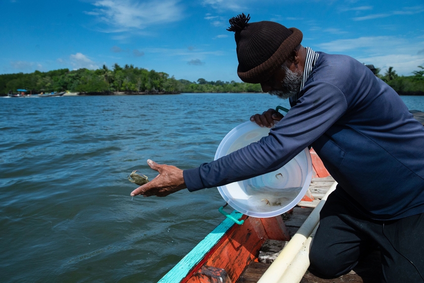 A man on a boat throws a crab into the sea.